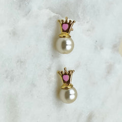 Pair of pearl earrings with gold crowns and pink centers on a white marble surface.